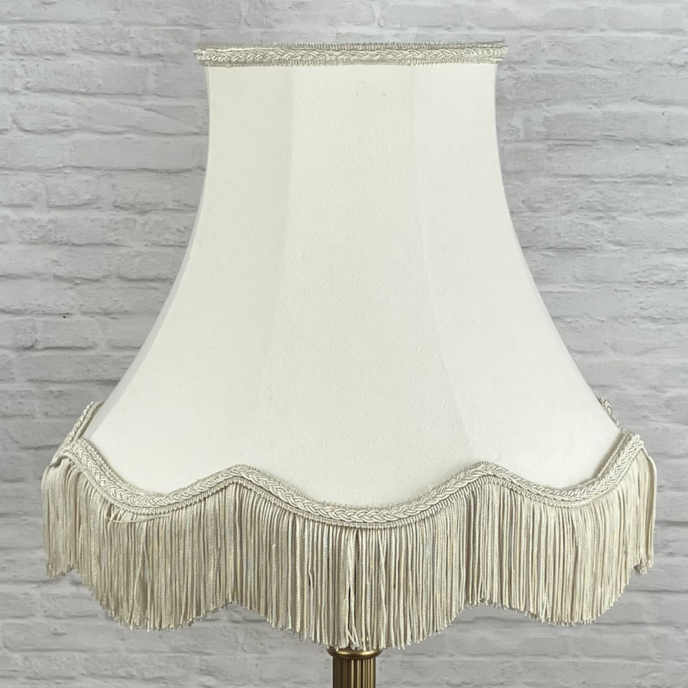Scalloped bowed empire lampshade in cream with a dark cream fringe on a table lamp switched off