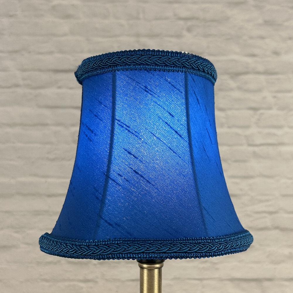 Blue bowed chandelier shade in faux silk lit showing rich tone and plait trim