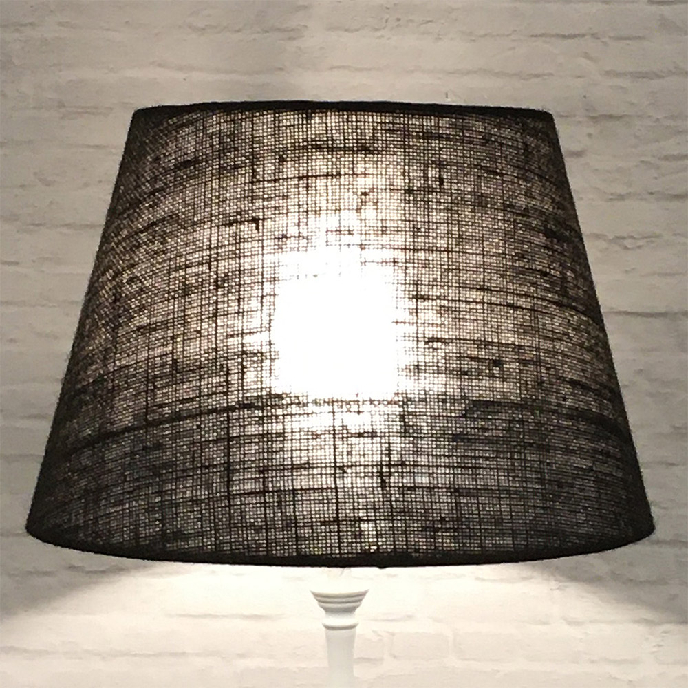 Brown hessian tapered drum lampshade lit on a white floor lamp base